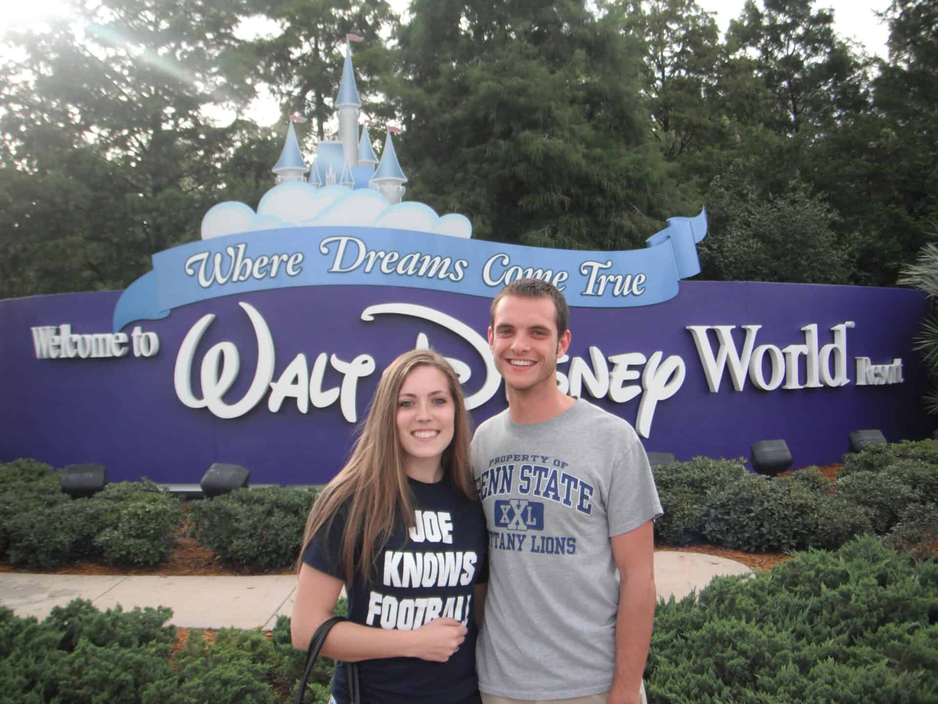 A man and woman standing in front of a Walt Disney World sign
