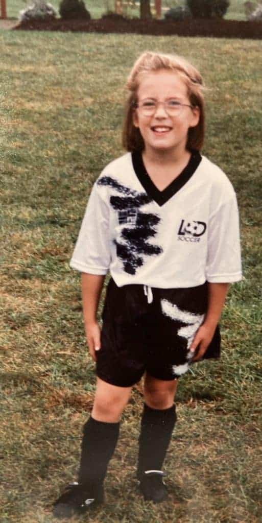 Little girl wearing glasses and a black and white soccer uniform