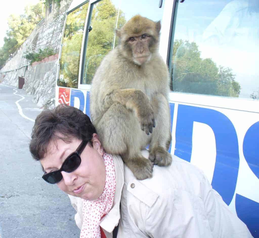 Woman wearing white coat and sunglasses with a monkey on her back