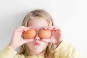 Young girl holding two brown eggs over her eyes