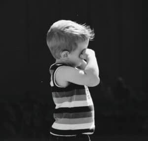 Black and white picture of a young boy rubbing his eyes