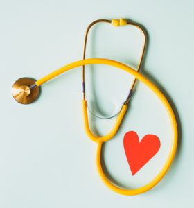 Yellow stethoscope with a red paper heart beside it and a light mint background.