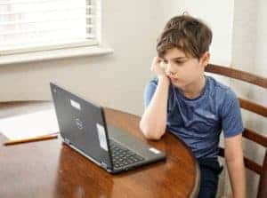 Young boy sitting at a wooden table in front of a gray computer