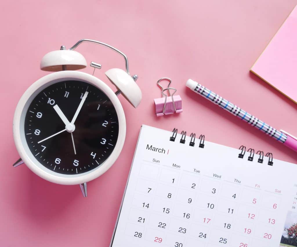 Black alarm clock with white calendar and pink background